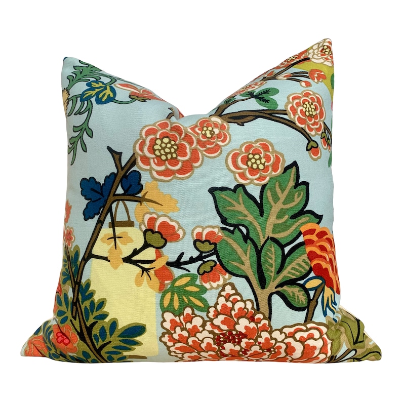 May include: A blue pillow with a floral pattern featuring red, orange, yellow, green, and blue flowers. The pillow has a light blue background and a white border.
