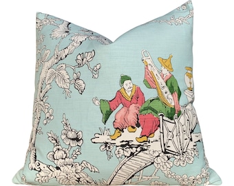 May include: A square throw pillow featuring a light blue background with a black and white toile-style print of trees and flowers. The design includes two figures in red and green clothing, one playing a long stringed instrument.