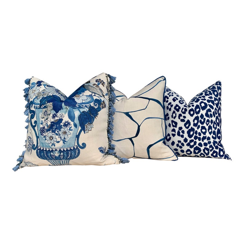 May include: Three decorative throw pillows with blue and white patterns. The first pillow has a blue and white floral design with a tassel trim. The second pillow has a white background with a blue geometric pattern. The third pillow has a white background with a blue leopard print.