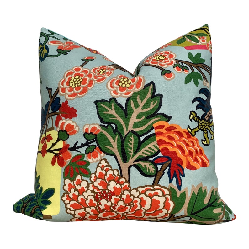 May include: Square throw pillow with a light blue background and a floral pattern. The design features large orange and red flowers, green leaves, and yellow accents. The pillow has a soft, inviting appearance.
