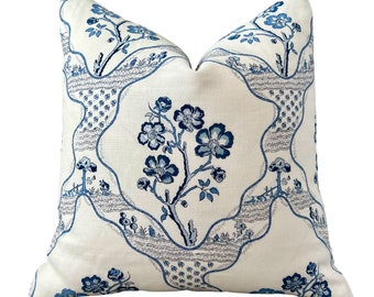 May include: A white cushion with a blue floral pattern. The pattern features stylised flowers and branches, and a repeating design of curved lines and dots.