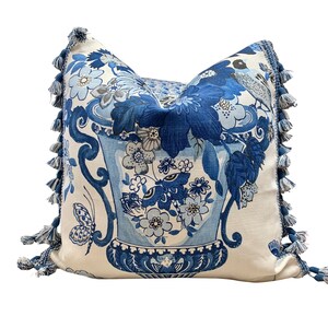 May include: Blue and white floral pillow with a tassel trim. The pillow features a large vase with flowers and butterflies.
