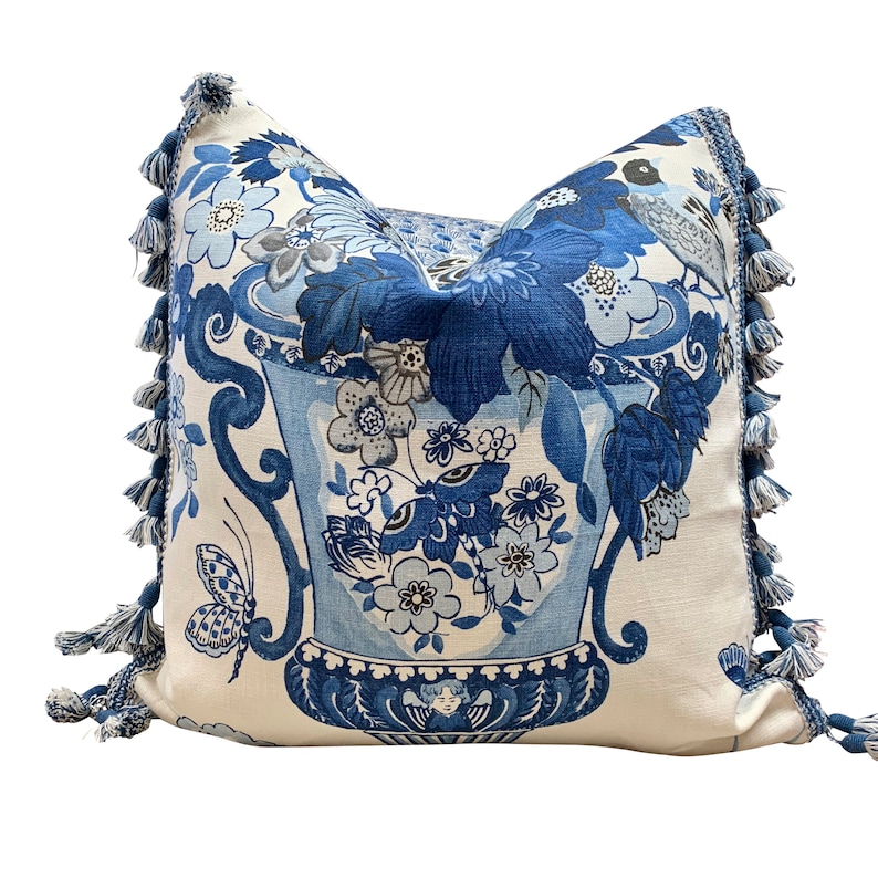 May include: Blue and white floral pillow with a tassel trim. The pillow features a large vase with flowers and butterflies.