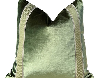 May include: A green velvet pillow with a white and green patterned trim. The pillow is rectangular and has a soft, plush texture.