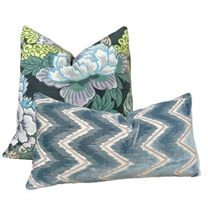 May include: Two decorative throw pillows. One pillow has a floral pattern in shades of green, blue, and purple on a black background. The other pillow is a solid blue with a white chevron pattern.