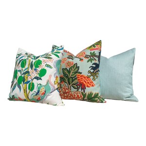 May include: Three decorative throw pillows. One pillow features a white background with green citrus fruit and foliage. Another has a light blue background with orange flowers and green leaves. The third pillow is a solid light blue.