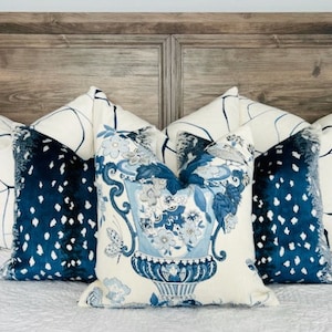 May include: A bed with a wooden headboard and a white duvet cover. There are five pillows on the bed, two with a white background and blue abstract designs, two with a blue background and white polka dots, and one with a white background and a blue floral design featuring a vase.