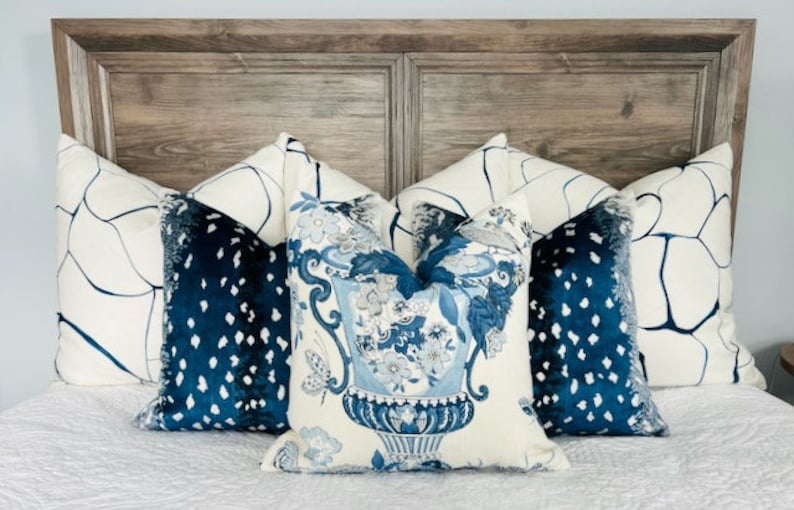 May include: A bed with a wooden headboard and a white duvet cover. There are five pillows on the bed, two with a white background and blue abstract designs, two with a blue background and white polka dots, and one with a white background and a blue floral design featuring a vase.