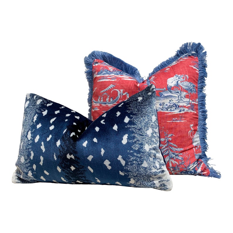 Pu&ograve; includere: Due cuscini decorativi, uno con un motivo geometrico blu e bianco e l'altro con un motivo floreale rosso e blu. Il cuscino floreale ha un bordo con frange.
