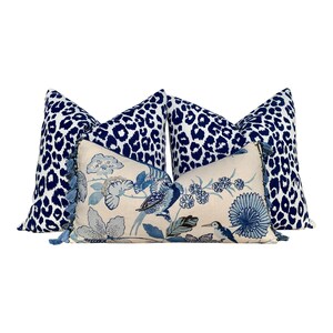 May include: Three decorative throw pillows with a blue and white floral pattern and a blue and white leopard print. The pillows have tassels on the edges.
