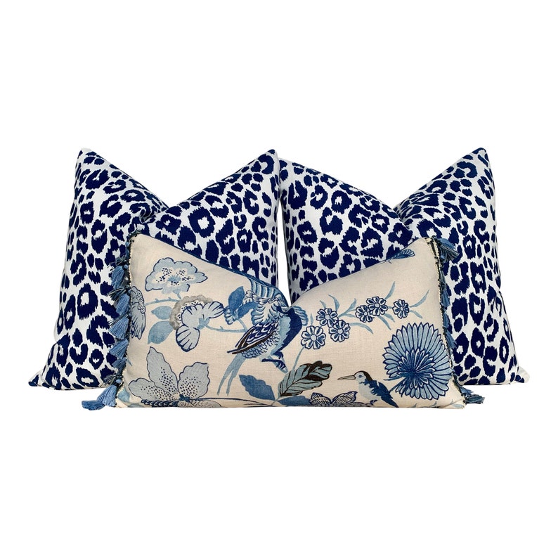 May include: Three decorative throw pillows with a blue and white floral pattern and a blue and white leopard print. The pillows have tassels on the edges.