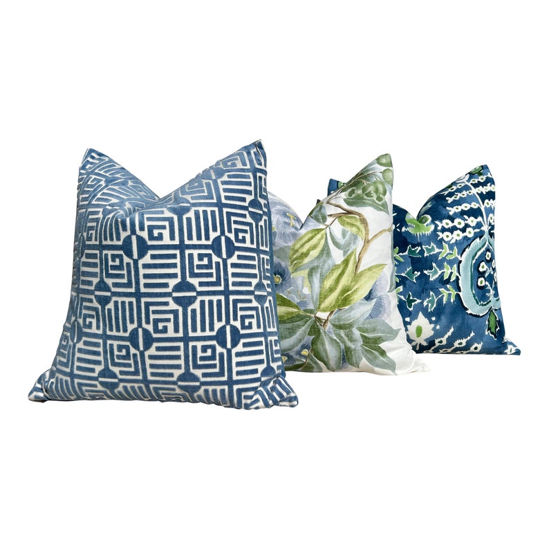 May include: Three decorative throw pillows with blue and green patterns. The pillow on the left has a geometric pattern in shades of blue. The middle pillow has a floral pattern with green leaves and blue flowers. The pillow on the right has a paisley pattern in shades of blue and green.