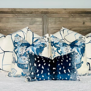 May include: A bed with a wooden headboard and a white duvet cover. There are five pillows on the bed, two with a white background and blue abstract designs, two with a white background and blue floral designs, and one with a blue background and white polka dots.