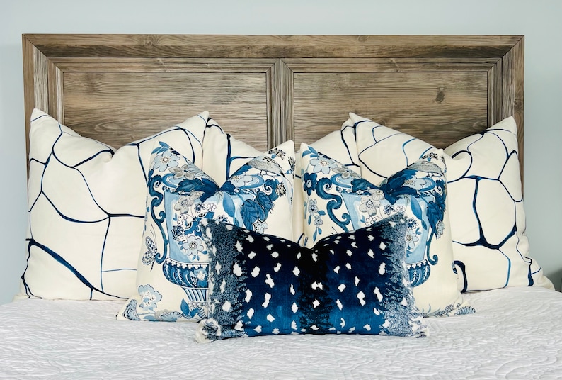 May include: A bed with a wooden headboard and a white duvet cover. There are five pillows on the bed, two with a white background and blue abstract designs, two with a white background and blue floral designs, and one with a blue background and white polka dots.