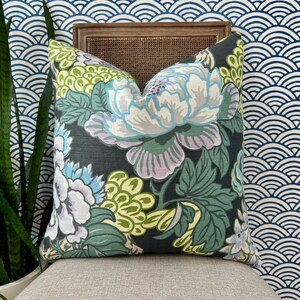 May include: A black pillow with a floral pattern featuring large white, purple, and green flowers. The pillow has a dark green background and is accented with light green and yellow details.