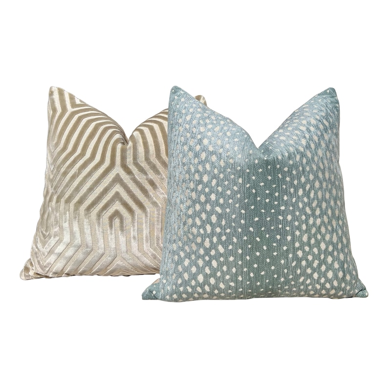 May include: Two decorative throw pillows, one with a geometric pattern in gold and beige, and the other with a white and blue patterned design.