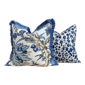 Pu&ograve; includere: Due cuscini decorativi con motivi blu e bianchi. Un cuscino presenta un disegno floreale con fiori e foglie blu su uno sfondo bianco. L'altro cuscino ha una stampa animalier blu e bianca. Entrambi i cuscini hanno un bordo con frange blu.