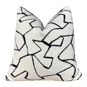 May include: A square decorative pillow with a white background and a bold black geometric pattern. The pillow has a textured surface and a soft appearance, suitable for home decor.