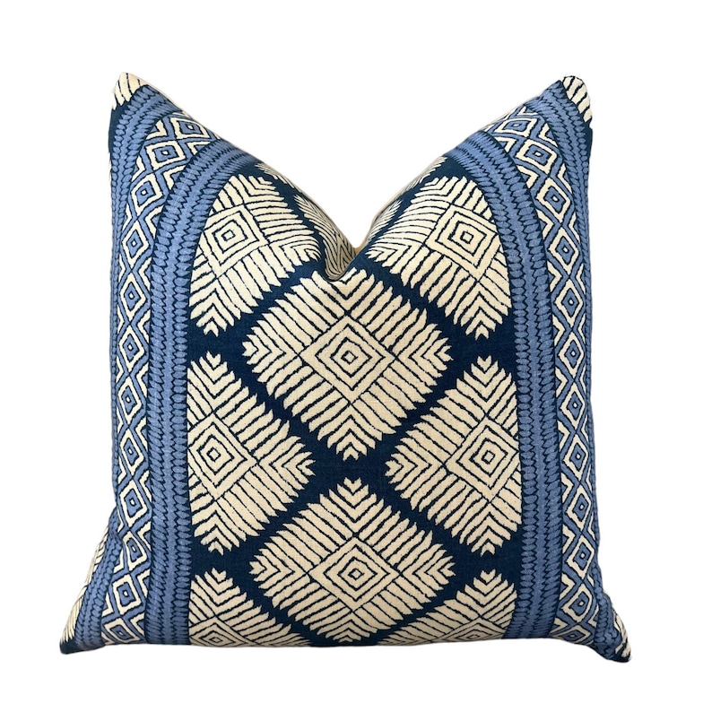 Puede incluir: Una almohada de tiro azul y blanco con un dise&ntilde;o geom&eacute;trico. La almohada tiene un borde azul claro con un patr&oacute;n de diamantes blancos.