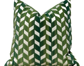 May include: A square decorative pillow with a repeating chevron pattern. The pattern alternates between white and shades of green. The pillow is made of a soft, textured fabric and is designed for home decor.