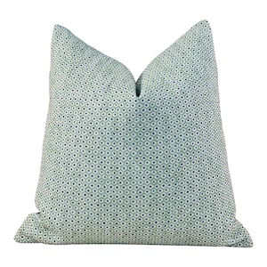 May include: A square throw pillow featuring a light sage green base color with a repeating pattern of small, dark blue diamond shapes outlined in white. The pillow has a soft, plump appearance with a distinct crease at the top center.