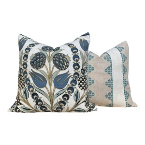 May include: Two decorative throw pillows. One pillow features a floral design in shades of blue, green, and tan on a white background. The second pillow has a tan background with a vertical stripe of white and teal geometric shapes.
