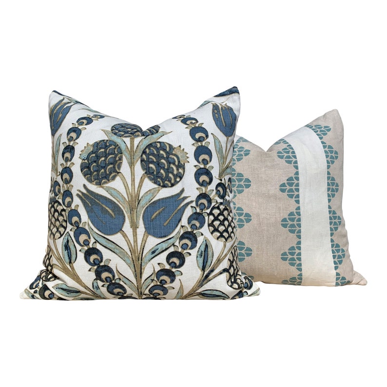 May include: Two decorative throw pillows. One pillow features a floral design in shades of blue, green, and tan on a white background. The second pillow has a tan background with a vertical stripe of white and teal geometric shapes.