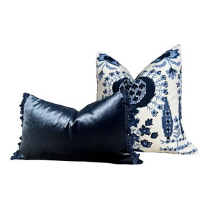 May include: Two decorative throw pillows, one with a blue and white floral pattern and the other a solid dark blue velvet.