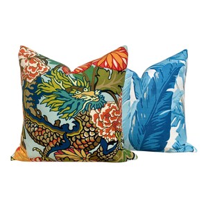 May include: Two decorative throw pillows with colorful patterns. One pillow features a blue background with a large green dragon and floral accents. The other pillow has a blue background with large white and blue leaves.