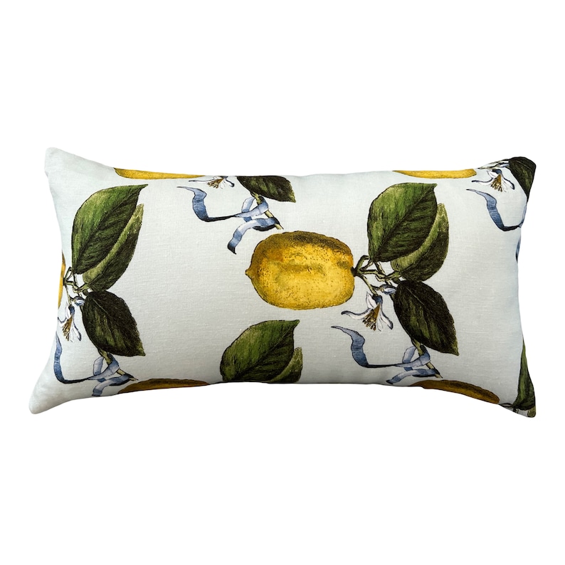 May include: Rectangular decorative pillow with a white background and a botanical lemon print. The print features yellow lemons, green leaves, and blue ribbons. The pillow is a light, neutral color.