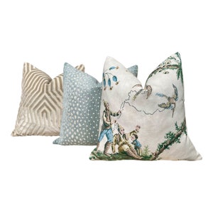 May include: Three decorative throw pillows with different patterns. The first pillow is a beige and brown geometric pattern. The second pillow is a light blue with white polka dots. The third pillow is a white background with a green and brown floral pattern and a scene of children playing with a kite.