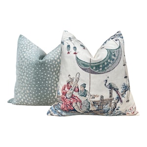 May include: Two decorative throw pillows with a light blue and white polka dot pattern and a cream background with a colorful Asian-inspired design featuring a peacock, two figures, and a boat.