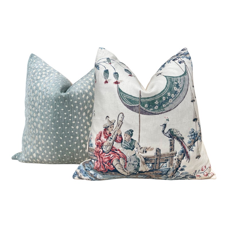 May include: Two decorative throw pillows with a light blue and white polka dot pattern and a cream background with a colorful Asian-inspired design featuring a peacock, two figures, and a boat.