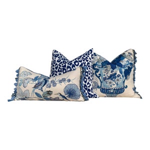 May include: Three decorative throw pillows with blue and white patterns. The pillows have tassels and are arranged in a row. The pillow on the left has a blue and white floral pattern with birds. The middle pillow has a blue and white leopard print. The pillow on the right has a blue and white floral pattern with a vase.