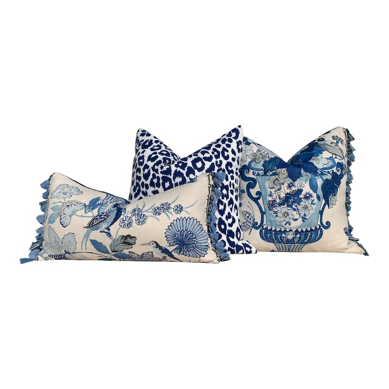 May include: Three decorative throw pillows with blue and white patterns. The pillows have tassels and are arranged in a row. The pillow on the left has a blue and white floral pattern with birds. The middle pillow has a blue and white leopard print. The pillow on the right has a blue and white floral pattern with a vase.