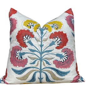 May include: A square cushion with a floral design. The cushion has a white background with a large, stylised floral pattern in red, pink, yellow, blue, and tan. The cushion appears to be made of a linen-like fabric.