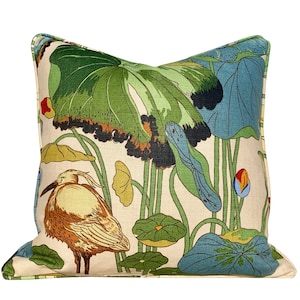 May include: A decorative throw pillow with a white background and a colorful floral pattern. The pattern features green, blue, and yellow lotus leaves, a brown and yellow bird, and a red and blue flower bud.