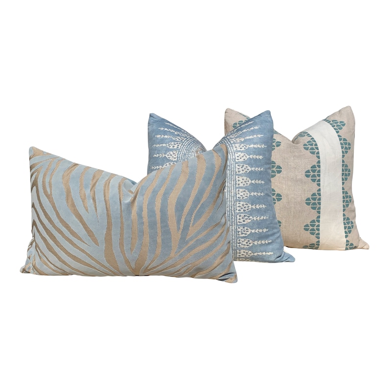 May include: Three decorative throw pillows in various designs. One pillow features a light blue background with tan zebra stripes. Another has a light blue background with a white and blue pattern. The third pillow has a beige background with a teal and white design.