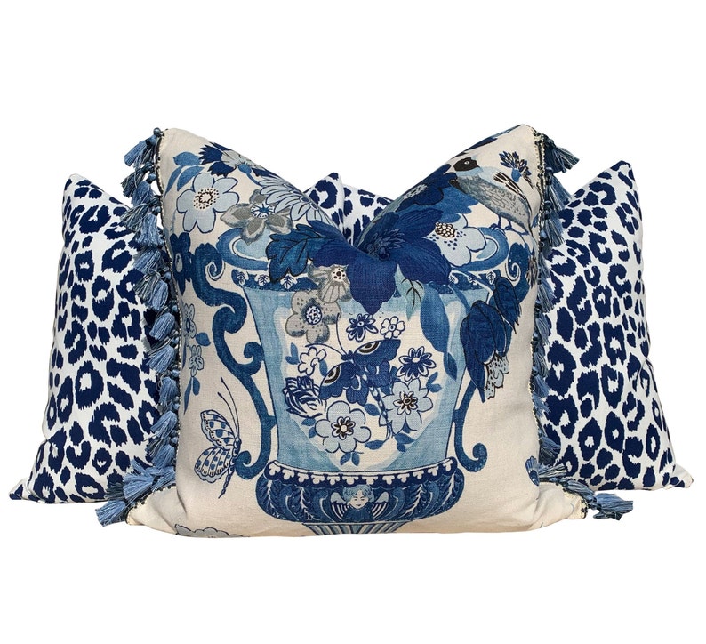 May include: Three decorative throw pillows with blue and white patterns. The center pillow features a blue and white floral design with a vase and butterflies. The two side pillows are blue and white leopard print with blue tassels.