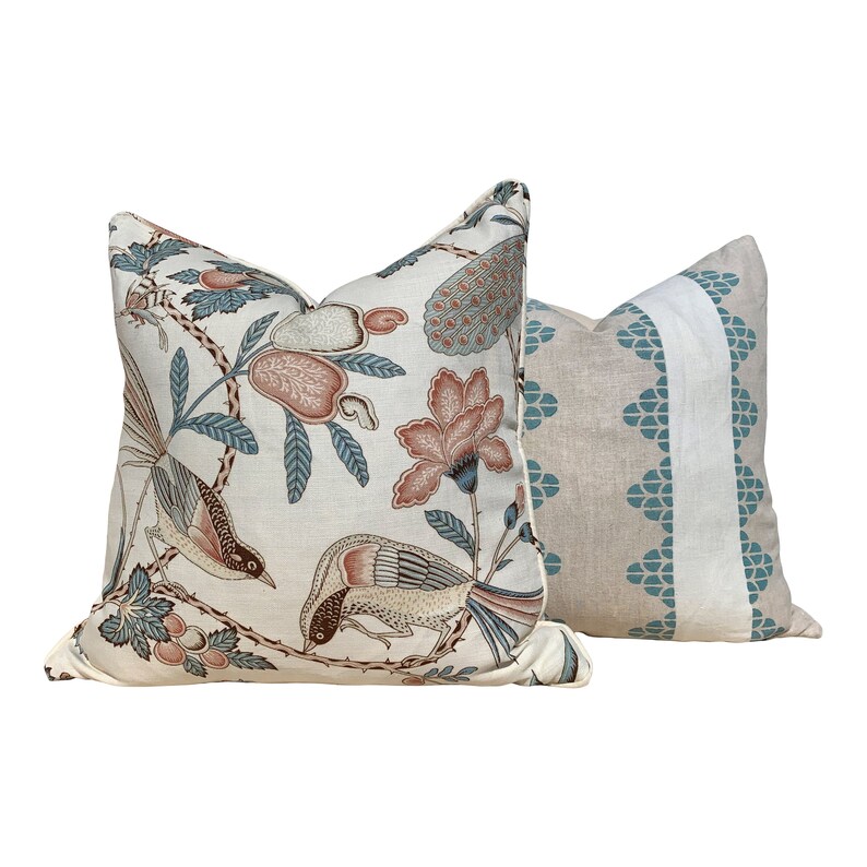 May include: Two decorative throw pillows. One features a cream background with a floral and bird pattern in shades of peach, teal, and brown. The other pillow has a beige background with a teal geometric design and a white stripe.