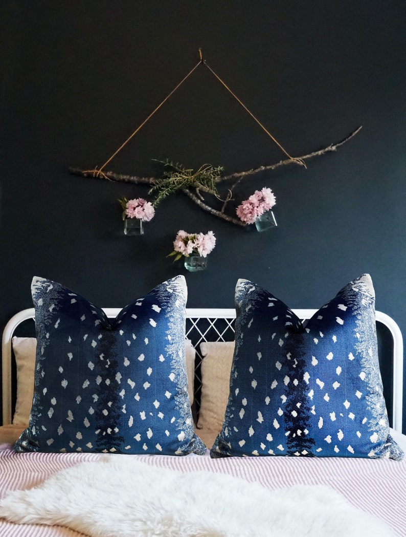 Pu&ograve; includere: Due cuscini da lancio blu e bianchi con un arrangiamento floreale bianco e rosa appeso a una parete blu scuro dietro i cuscini.