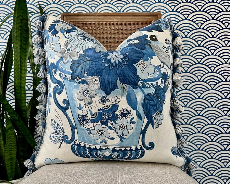 May include: Blue and white floral pillow with tassel trim. The pillow features a vase with flowers and butterflies.