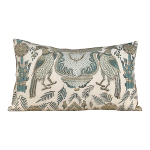 May include: A rectangular throw pillow with a white background and a blue and green floral pattern. The pattern features two peacocks with their tails spread out, a vase with a floral design, and leafy branches.