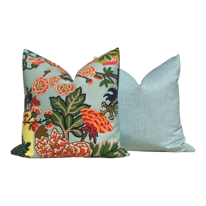 May include: Two decorative throw pillows. One features a light blue background with a floral pattern in orange, red, green, and yellow. The other pillow is a solid light blue with a textured appearance. Home decor.