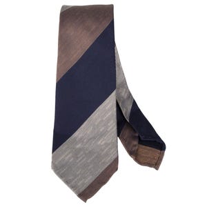 Peut inclure: Une cravate à rayures diagonales dans les tons de marron, bleu marine et gris. La cravate présente un design classique avec une extrémité pointue. Le tissu semble avoir une texture subtile, ajoutant un intérêt visuel à l'accessoire.