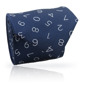 May include: A rolled navy blue tie featuring a white number design. The numbers are randomly placed across the tie's surface. The tie is made of a smooth fabric and is shown against a white backdrop.