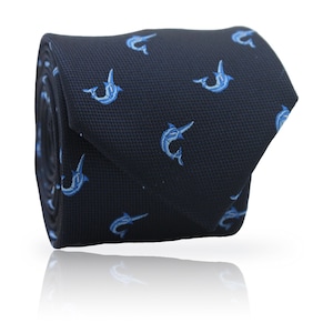 May include: Rolled navy blue tie with a repeating pattern of light blue marlin fish. The tie is made of a textured fabric and is displayed on a white background with a reflection.