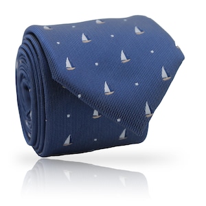 Puede incluir: Corbata azul marino enrollada con un patrón repetido de pequeños veleros blancos y puntos blancos. Los veleros tienen cascos de color beige. La corbata es de tela lisa y está enrollada.