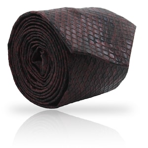 Peut inclure: Cravate enroulée avec un motif texturé semblable à celui d'un reptile, dans des tons bordeaux et noirs. La cravate est enroulée serrée, mettant en valeur la surface détaillée et les variations de couleur. L'extrémité de la cravate est visible, affichant le même motif.