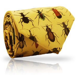 May include: A rolled yellow necktie with a repeating pattern of detailed insect illustrations in black, red, and green. The tie is made of a smooth fabric, suitable for formal or casual wear. The tie is rolled up.